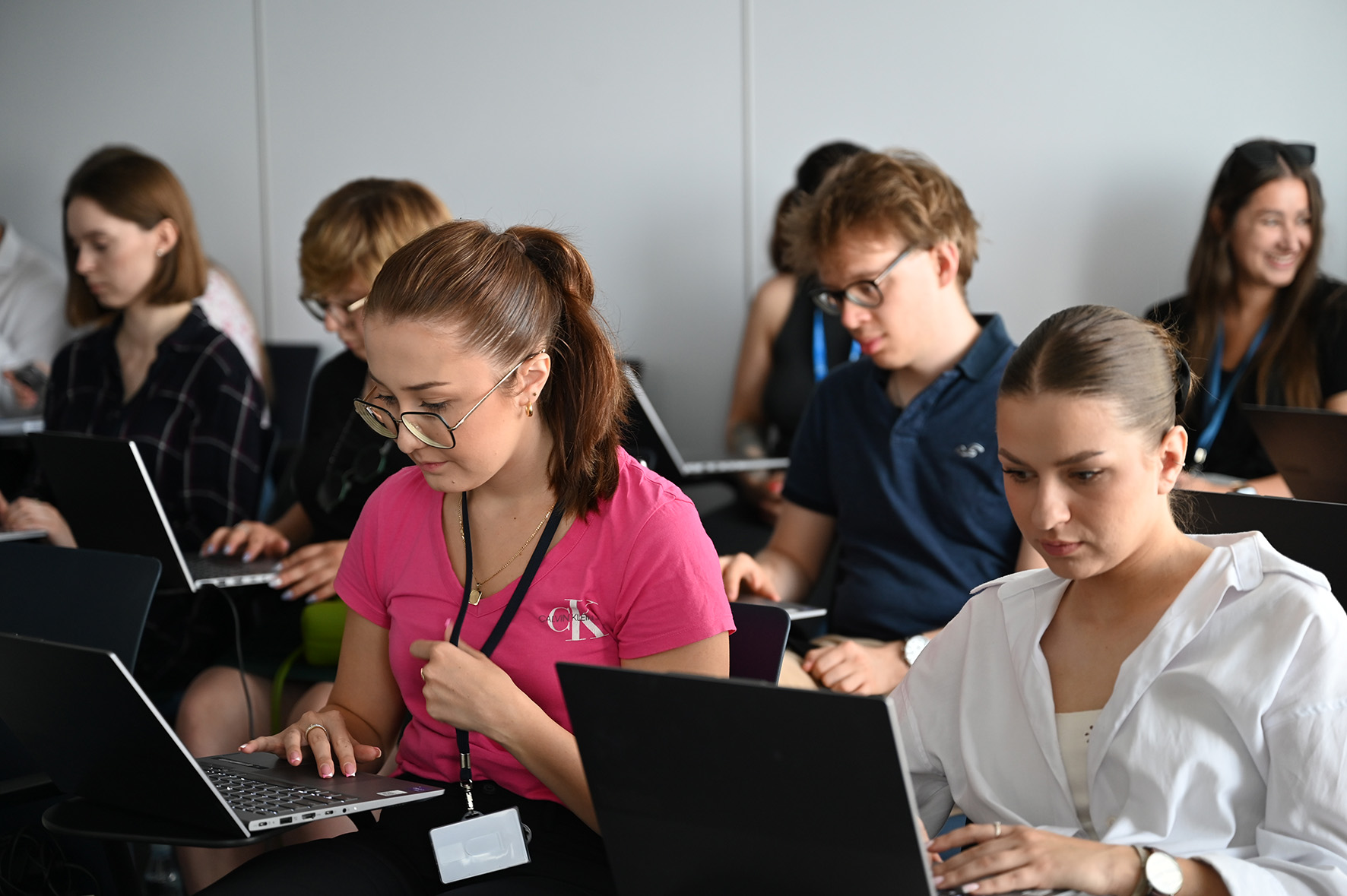 Studenci siedzą w sali i czytają informacje z laptopów.